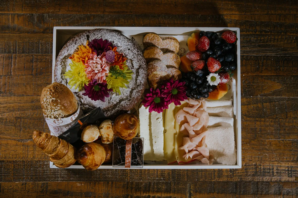 Cesta de café da manhã com bolo, pães, frutas e flores