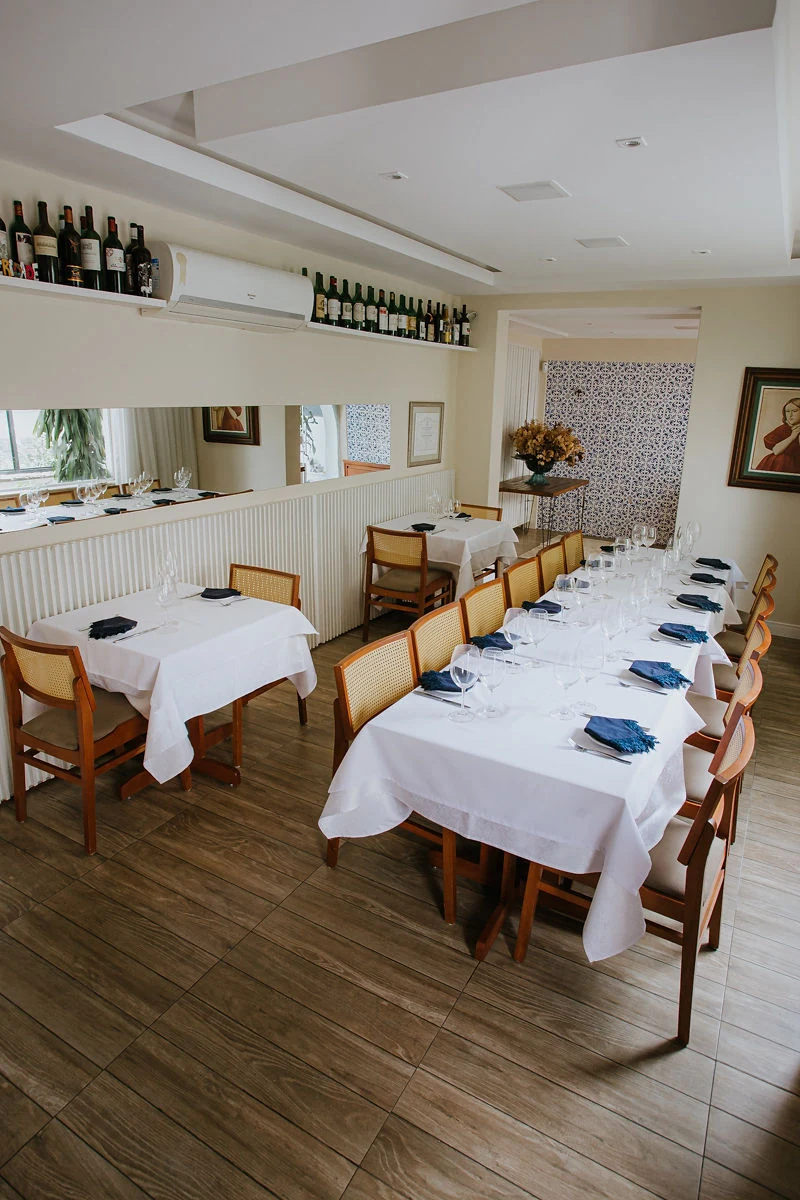 Salão do bistrô com mesas de toalha branca e prateleira de vinhos
